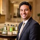 Dueño de hotel sonriendo en el lobby con amenities artesanales sobre una mesa
